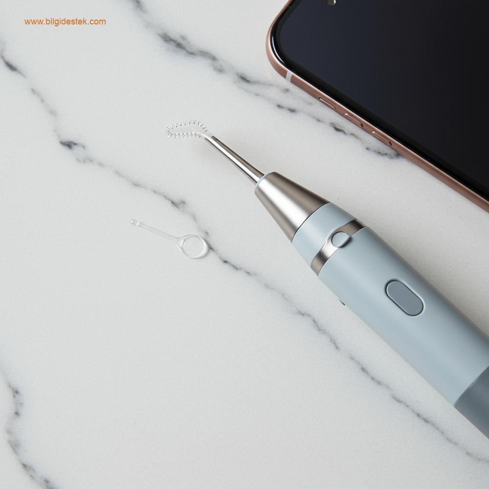 Yüksek teknoloji ürünü, endoskopik bir kulak temizleme cihazının üstten (flat lay) çekilmiş fotoğrafı. Temiz kamera ucu, yumuşak bir LED ışık kaynağının yanında duruyor ve görsel rehberlik yönü vurgulanıyor.